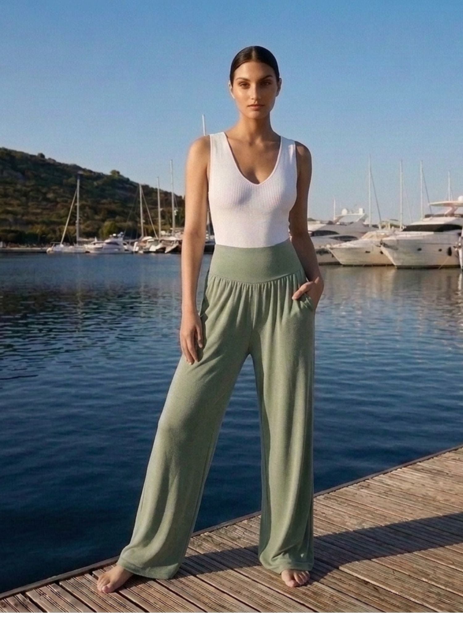 Woman in sage green wide-leg pants and white top on dock by marina, ideal for travel and everyday comfort