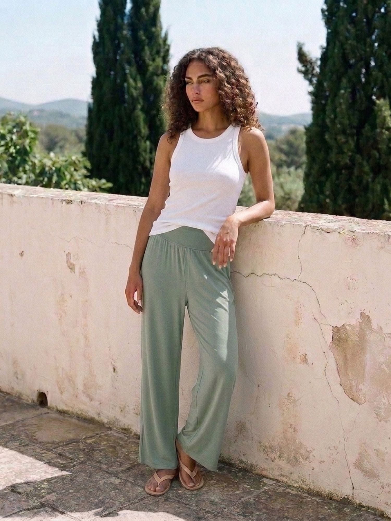 Woman in soft sage green wide-leg lounge pants and white tank top, ideal for travel or home comfort.