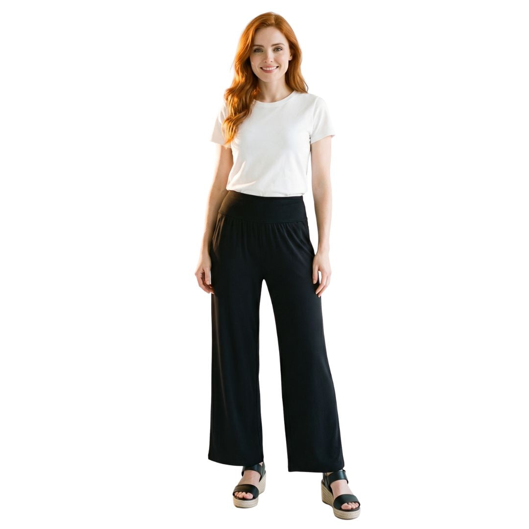 Woman wearing black wide-leg travel pants with elastic waist, paired with white tee and sandals