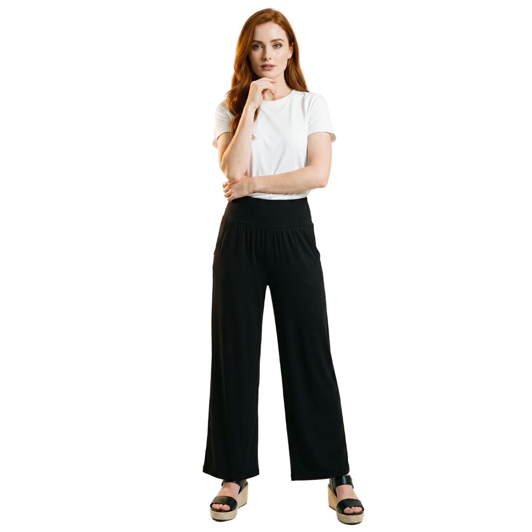 Woman wearing black wide-leg travel pants with elastic waist, paired with white tee and wedge sandals