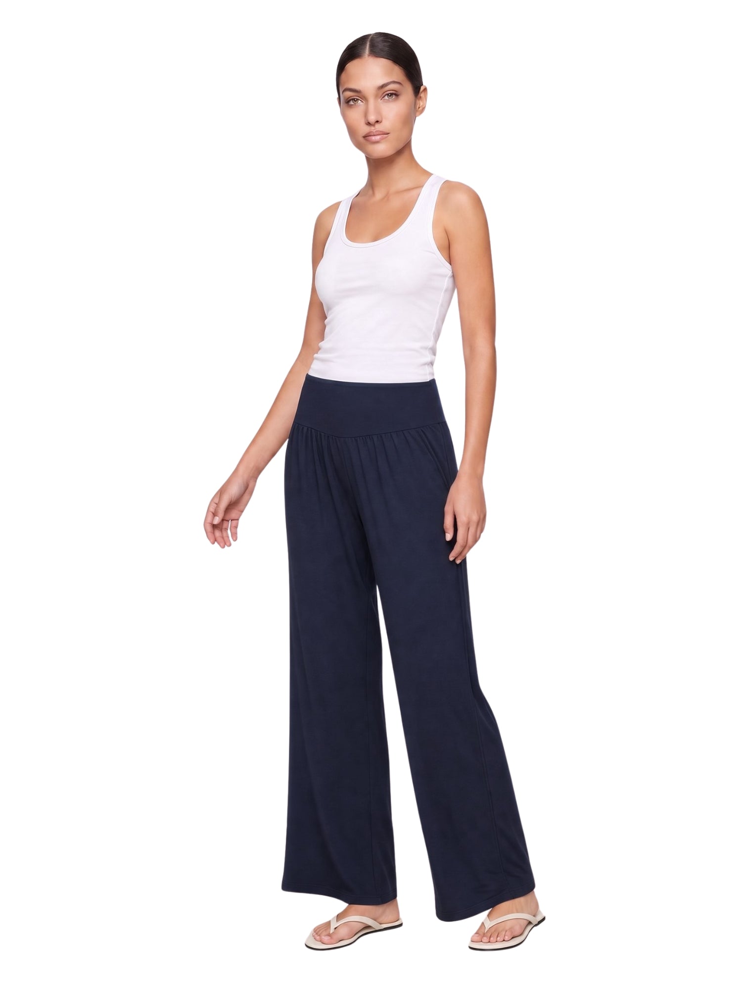 Woman wearing navy wide-leg lounge pants with elastic waist, paired with white tank top and flip flops
